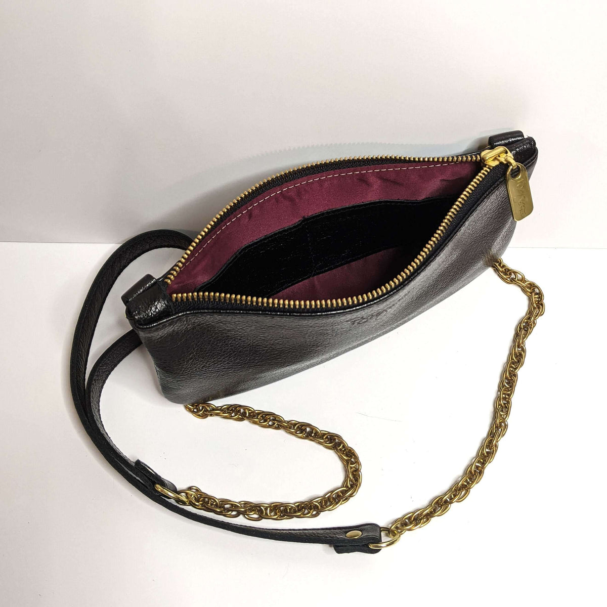 Open view of the Cher Chain Crossbody - Onyx, a metallic leather bag featuring a gold chain strap.
