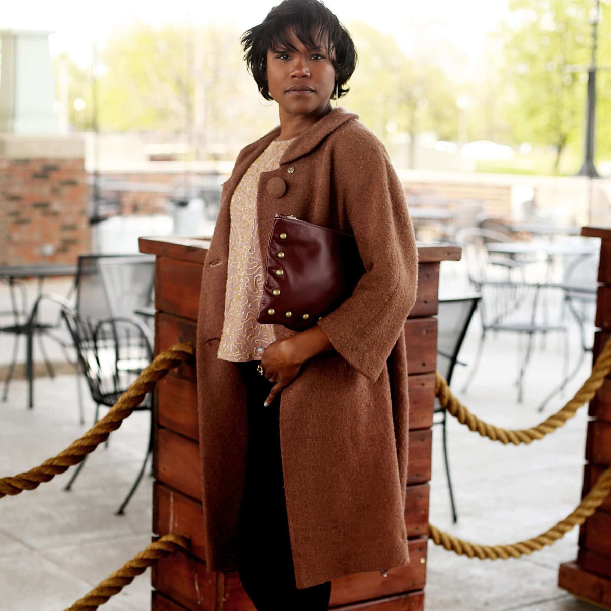 Woman wearing plum studded crossbody bag in full-grain leather as a clutch in city restaurant