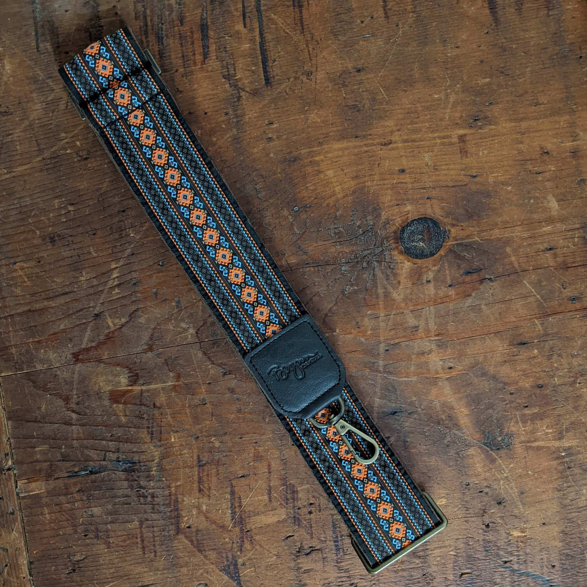 Lizzy Guitar Bag Strap - Diamonds with leather trim and woven prints on wooden background.